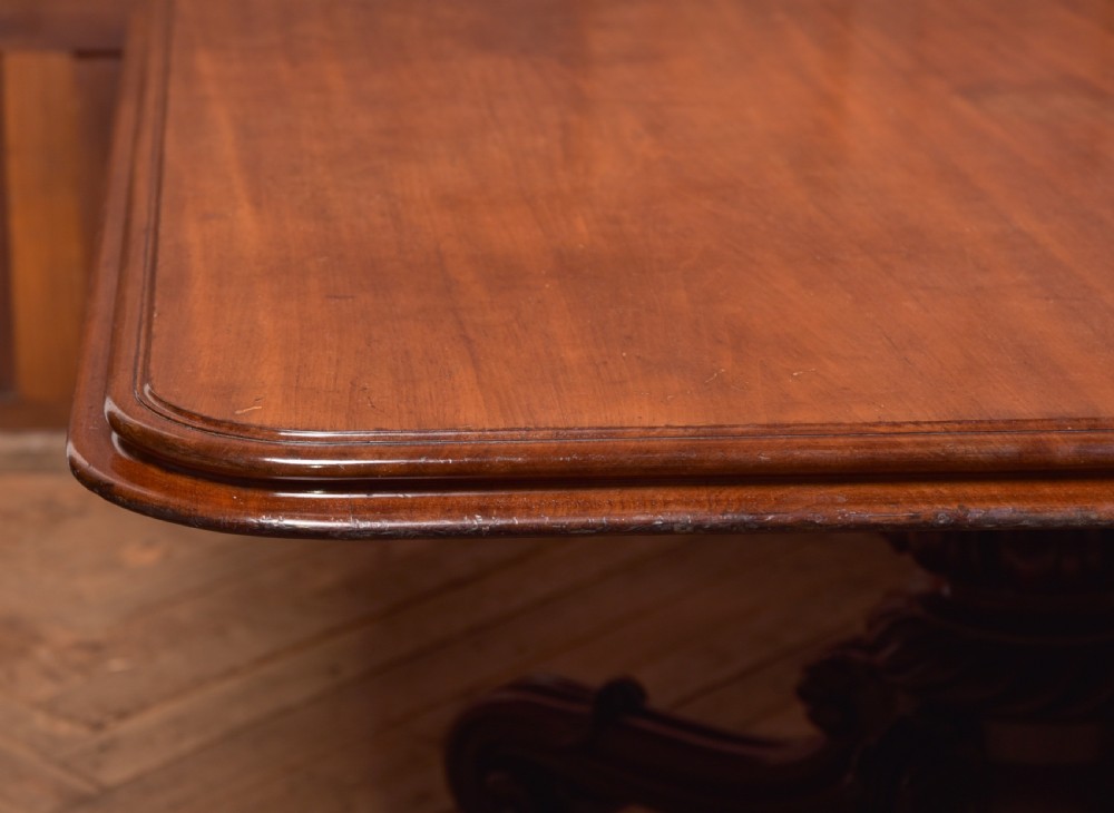 A Victorian mahogany tilt-top table featuring a polished rectangular top with rounded corners set upon a carved pedestal stem with quadruped scrolled legs. View II
