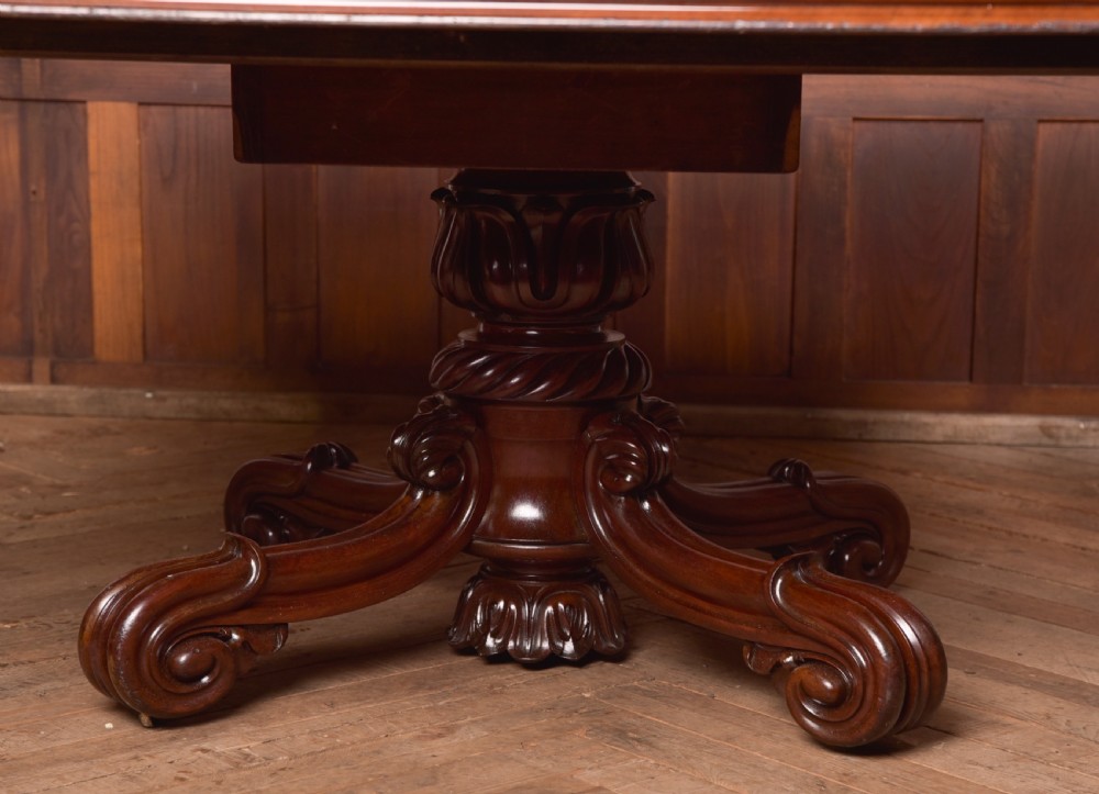 A Victorian mahogany tilt-top table featuring a polished rectangular top with rounded corners set upon a carved pedestal stem with quadruped scrolled legs. View V
