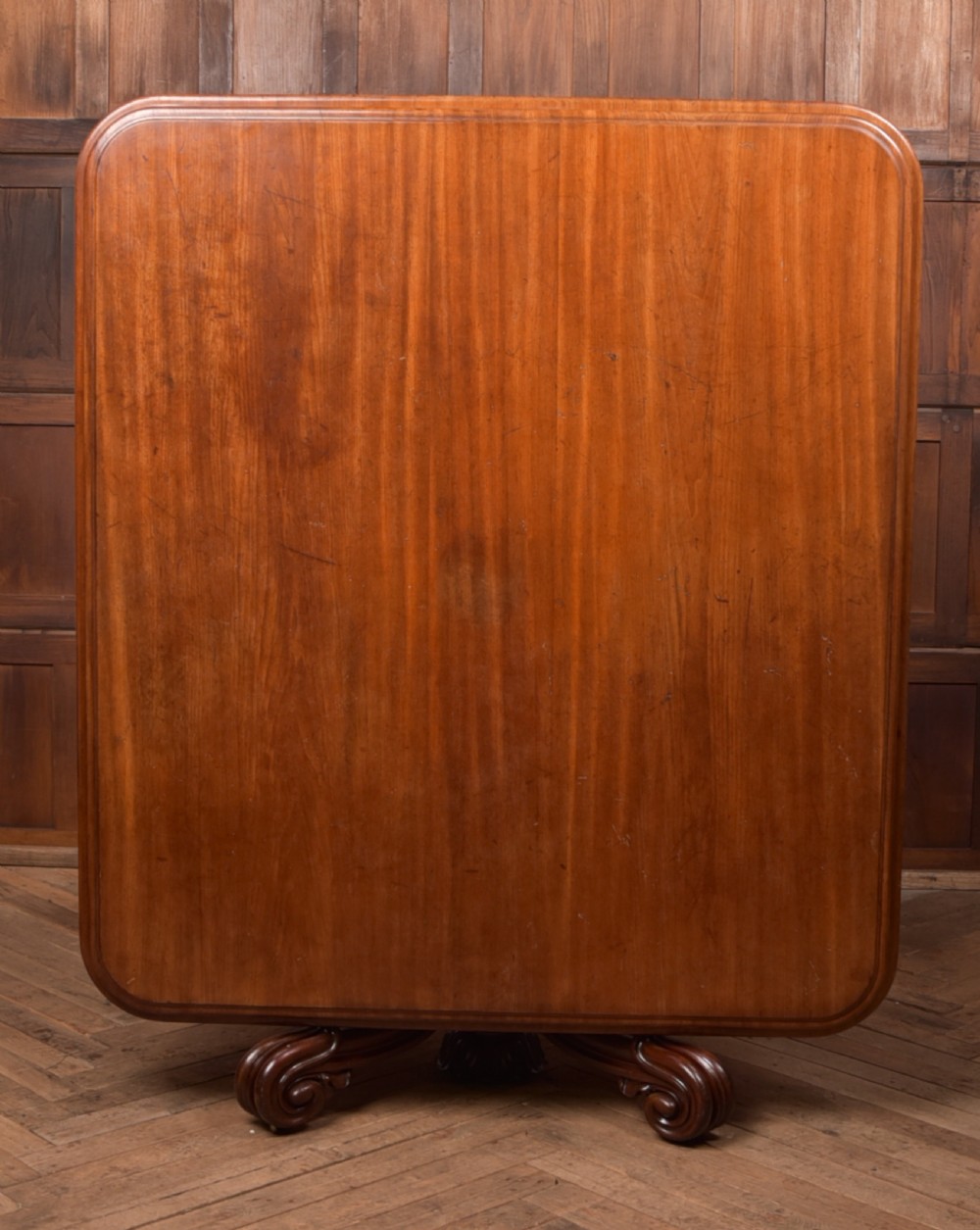 A Victorian mahogany tilt-top table featuring a polished rectangular top with rounded corners set upon a carved pedestal stem with quadruped scrolled legs. View VI