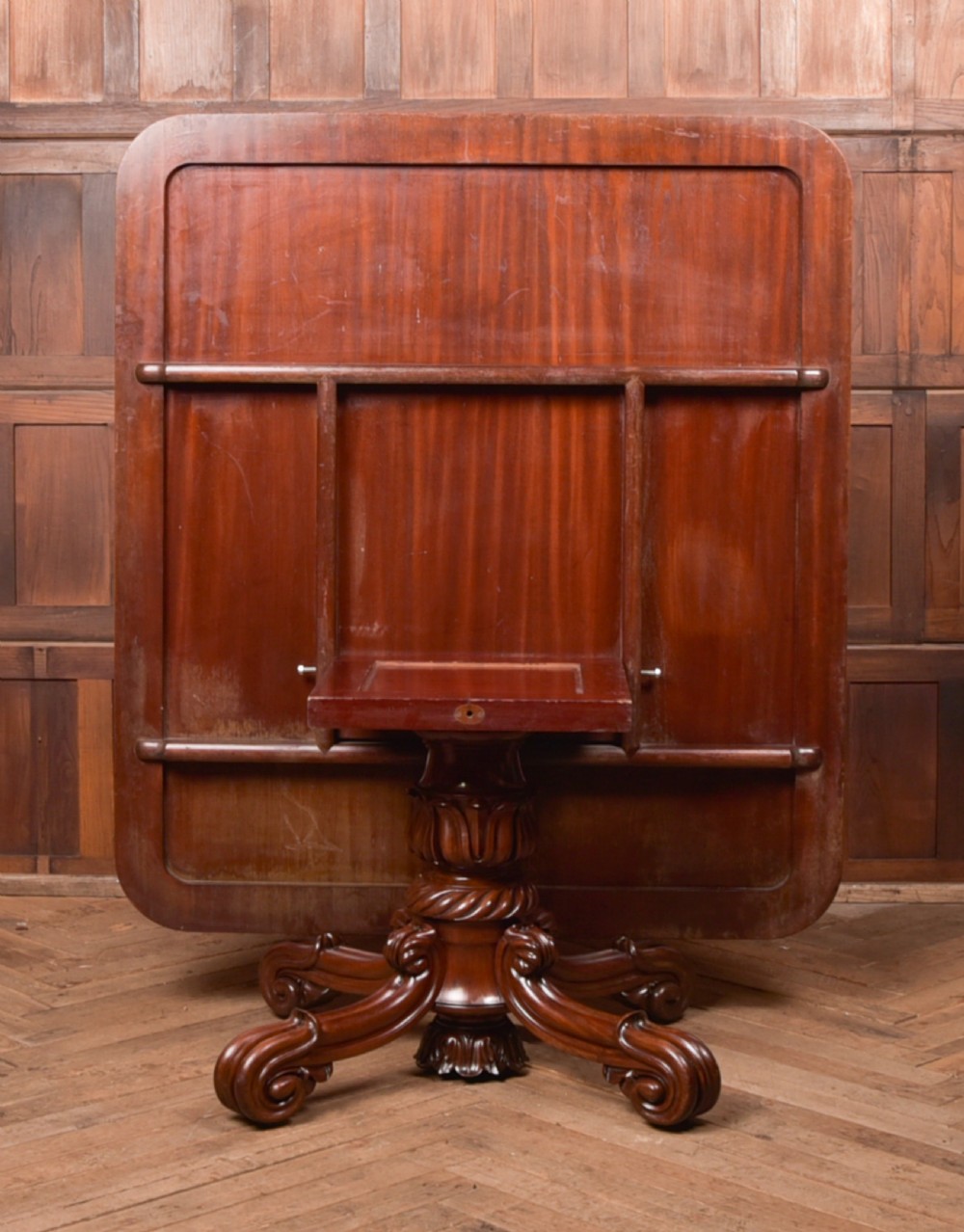 A Victorian mahogany tilt-top table featuring a polished rectangular top with rounded corners set upon a carved pedestal stem with quadruped scrolled legs. View VIII