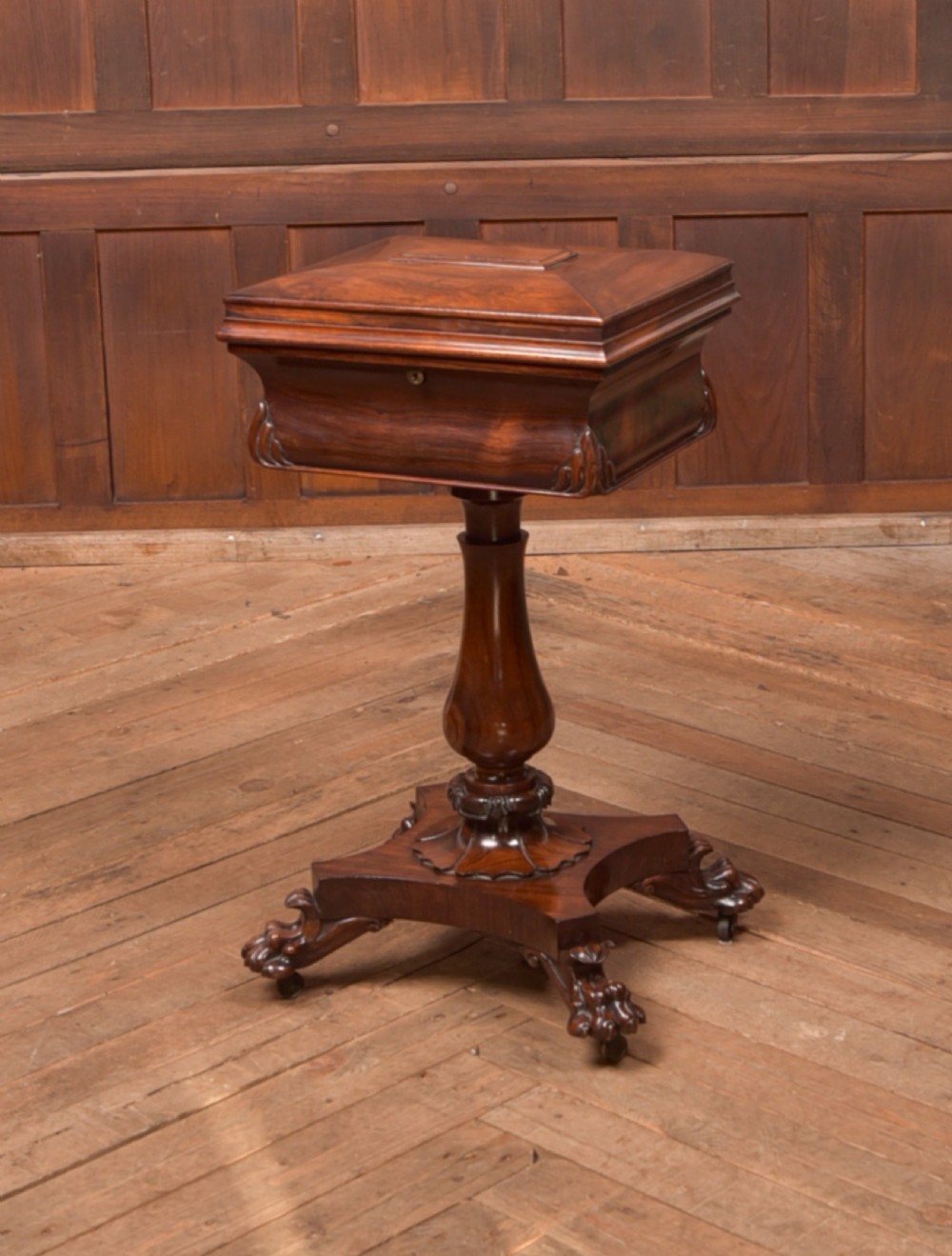 A Victorian rosewood work table featuring a hinged sarcophagus lid, a turned pedestal column, and a carved quadruped base on brass castors.