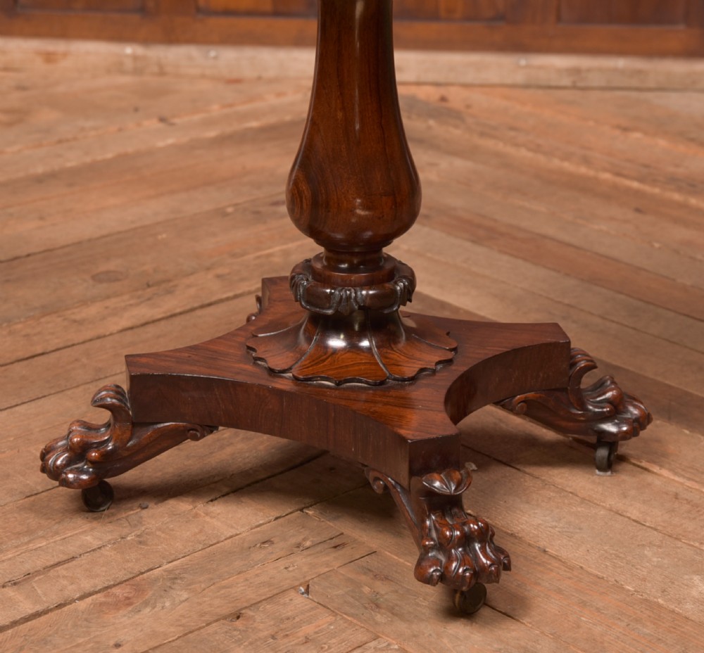 A Victorian rosewood work table featuring a hinged sarcophagus lid, a turned pedestal column, and a carved quadruped base on brass castors. View V