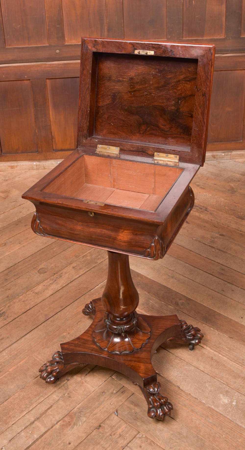 A Victorian rosewood work table featuring a hinged sarcophagus lid, a turned pedestal column, and a carved quadruped base on brass castors. View VI