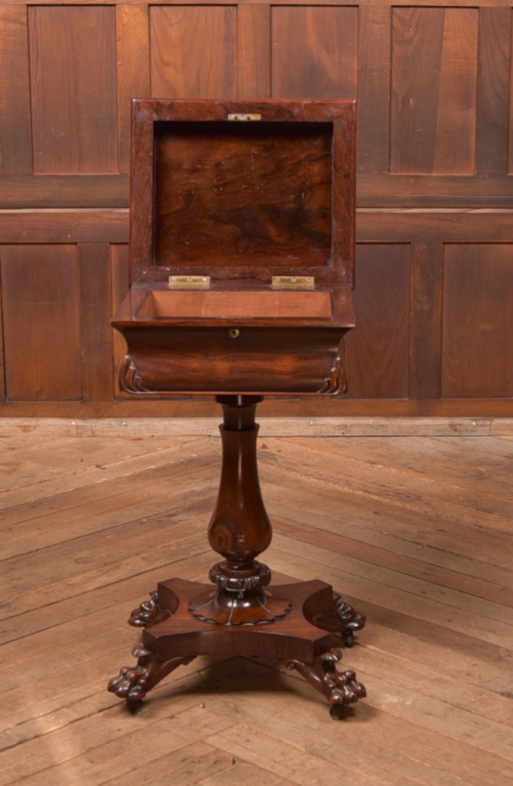 A Victorian rosewood work table featuring a hinged sarcophagus lid, a turned pedestal column, and a carved quadruped base on brass castors. View VII