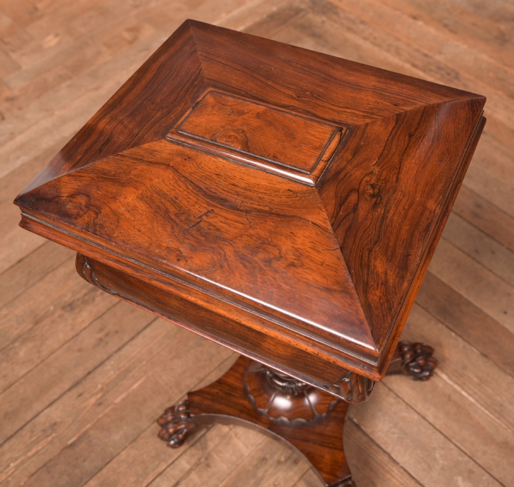 A Victorian rosewood work table featuring a hinged sarcophagus lid, a turned pedestal column, and a carved quadruped base on brass castors. View IX