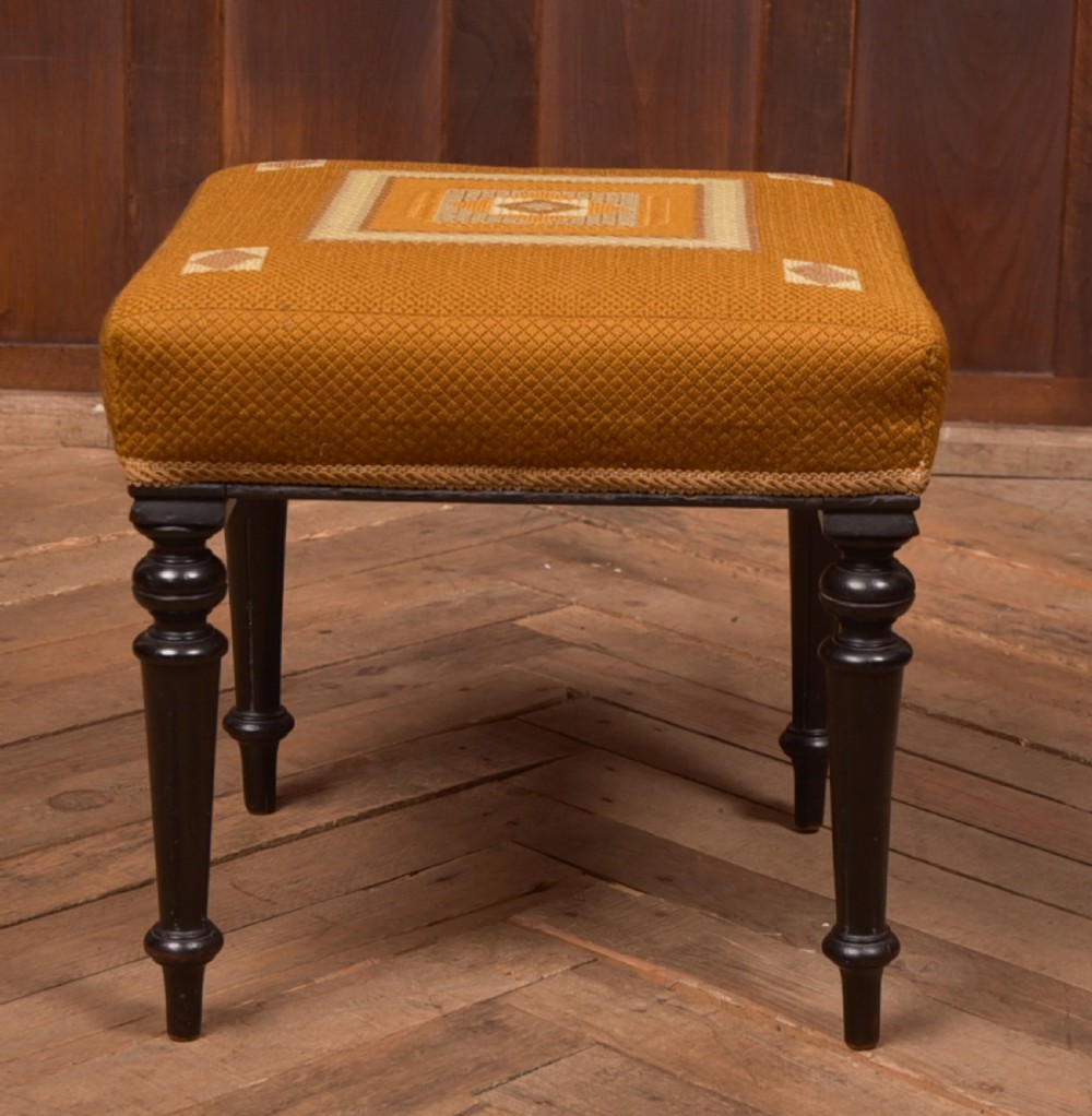 A Victorian rectangular footstool featuring black turned ebonised legs and an ochre yellow geometric needlepoint upholstered top.