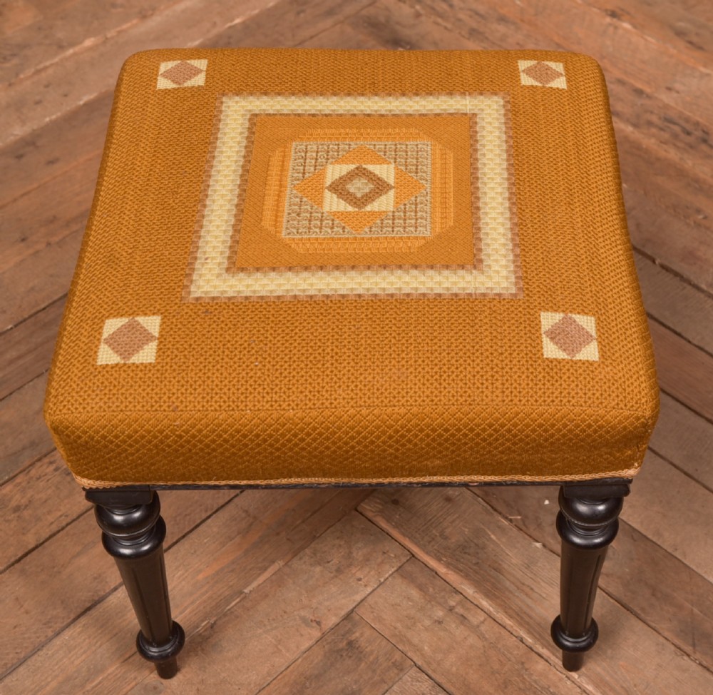 A Victorian rectangular footstool featuring black turned ebonised legs and an ochre yellow geometric needlepoint upholstered top. View II