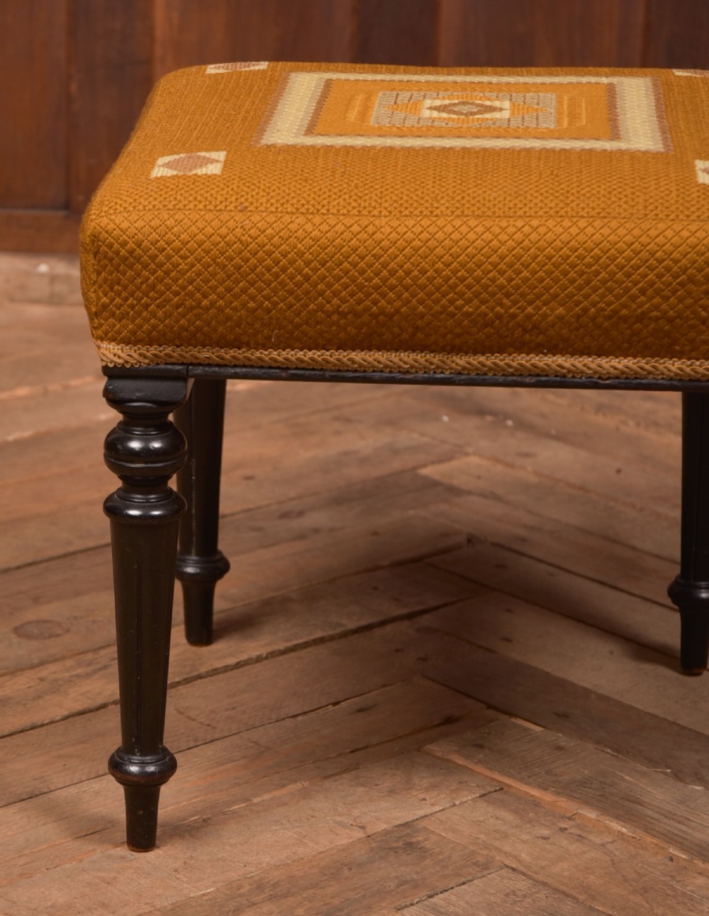 A Victorian rectangular footstool featuring black turned ebonised legs and an ochre yellow geometric needlepoint upholstered top. View V
