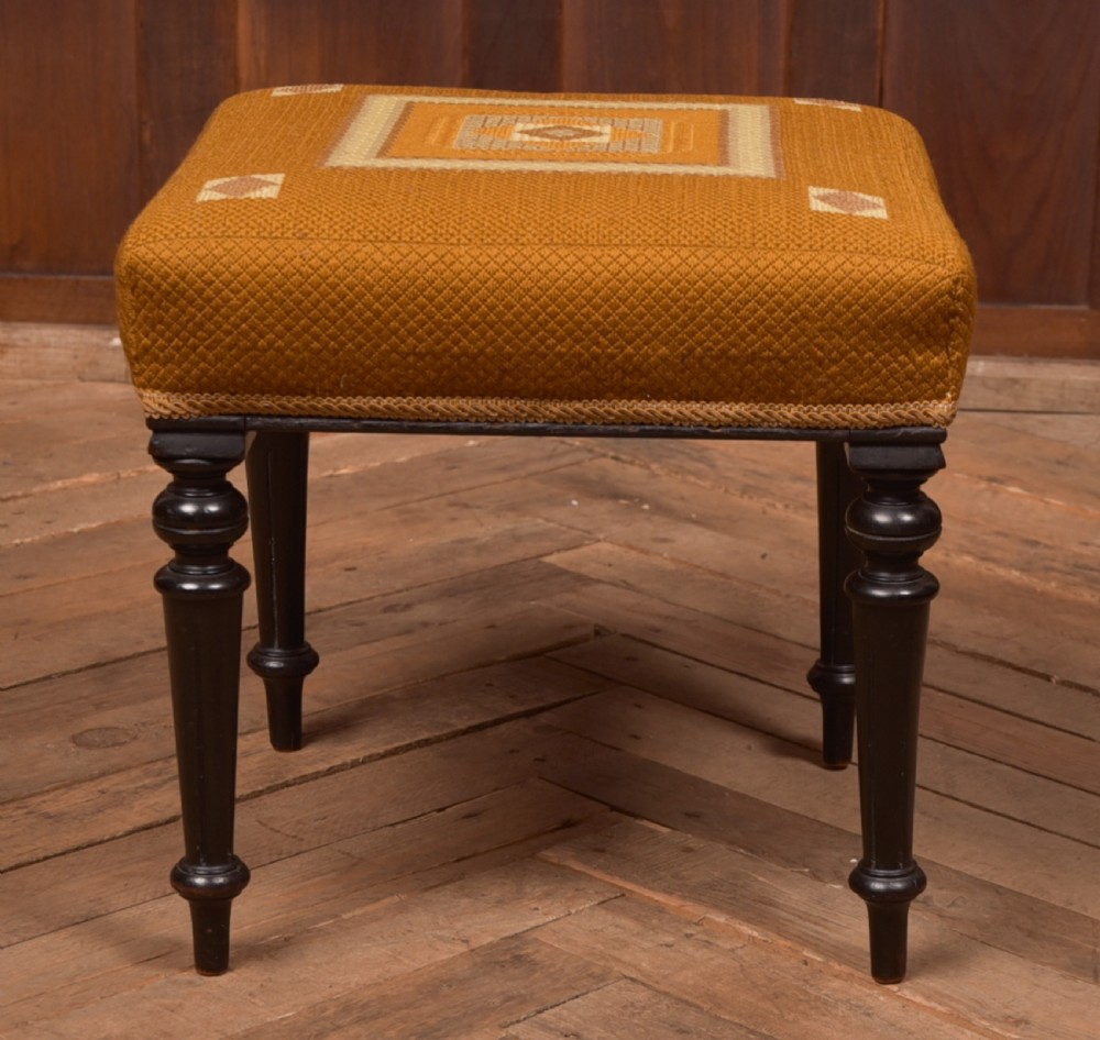 A Victorian rectangular footstool featuring black turned ebonised legs and an ochre yellow geometric needlepoint upholstered top. View VI