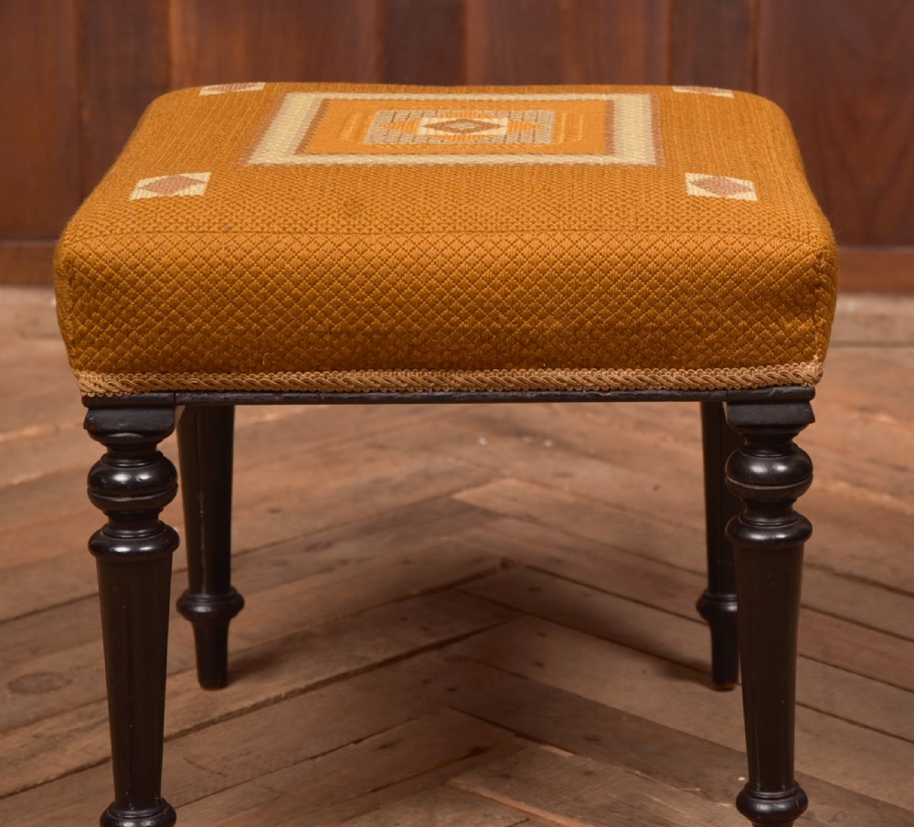 A Victorian rectangular footstool featuring black turned ebonised legs and an ochre yellow geometric needlepoint upholstered top. View IX