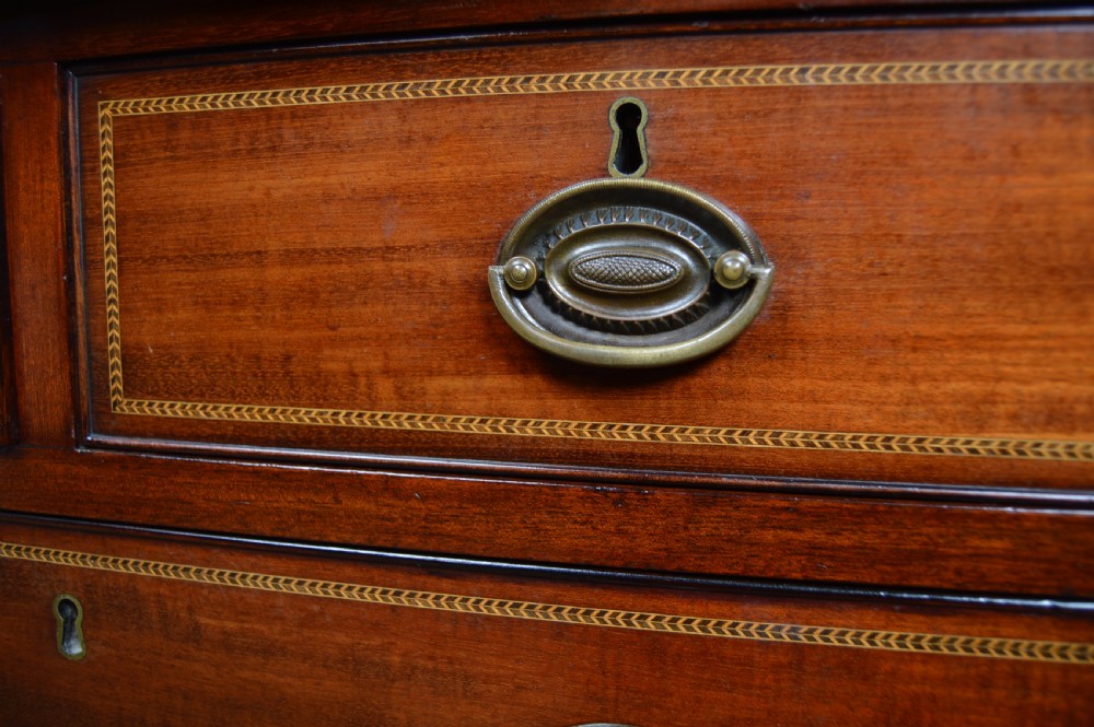 An Edwardian mahogany chest of drawers featuring two short over three long drawers with boxwood stringing inlay, brass oval drop handles, and bracket feet. View XXI