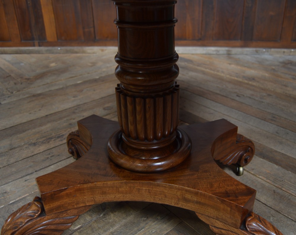 A William IV mahogany fold-over tea table featuring a swivelling top, a fluted turned central pedestal, and a quadform base with scroll feet on brass castors. View XII