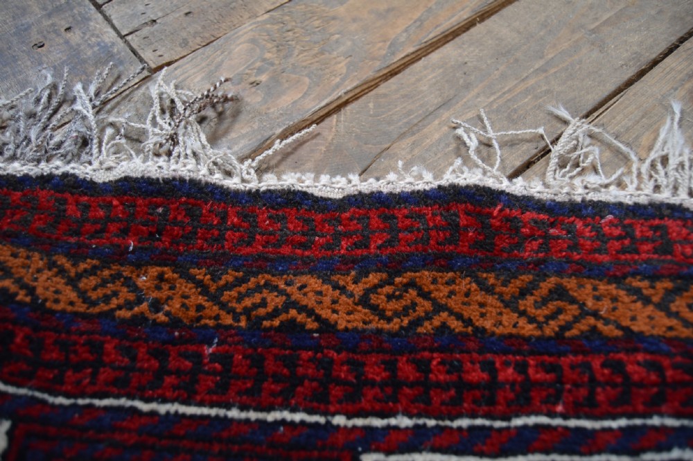 A hand-woven Belouch wool prayer rug featuring a central ochre mihrab motif surrounded by dark red and geometric patterned borders. View VI