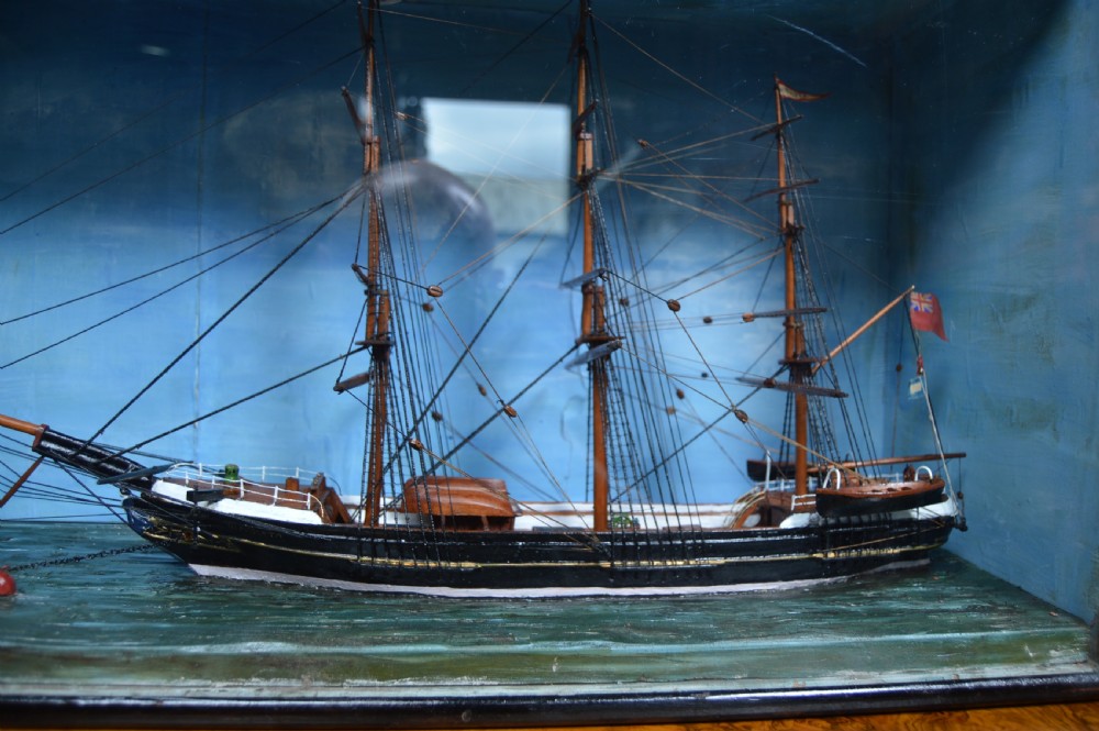 A detailed three-masted clipper ship model with fine thread rigging set against a painted sea and sky inside a black glazed display case. View III