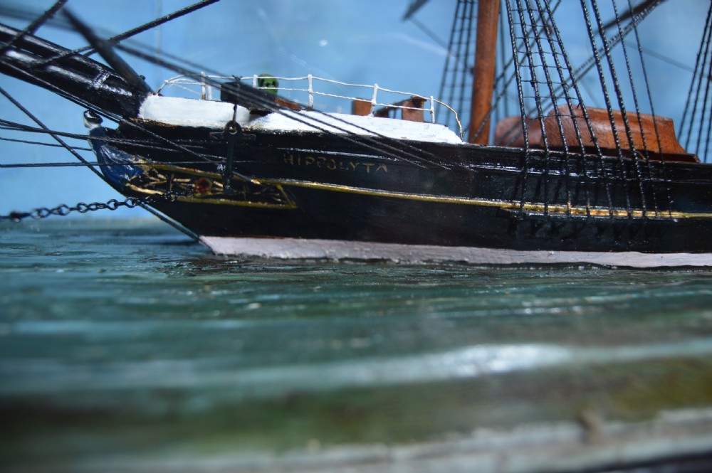 A detailed three-masted clipper ship model with fine thread rigging set against a painted sea and sky inside a black glazed display case. View IV
