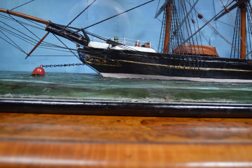 A detailed three-masted clipper ship model with fine thread rigging set against a painted sea and sky inside a black glazed display case. View V