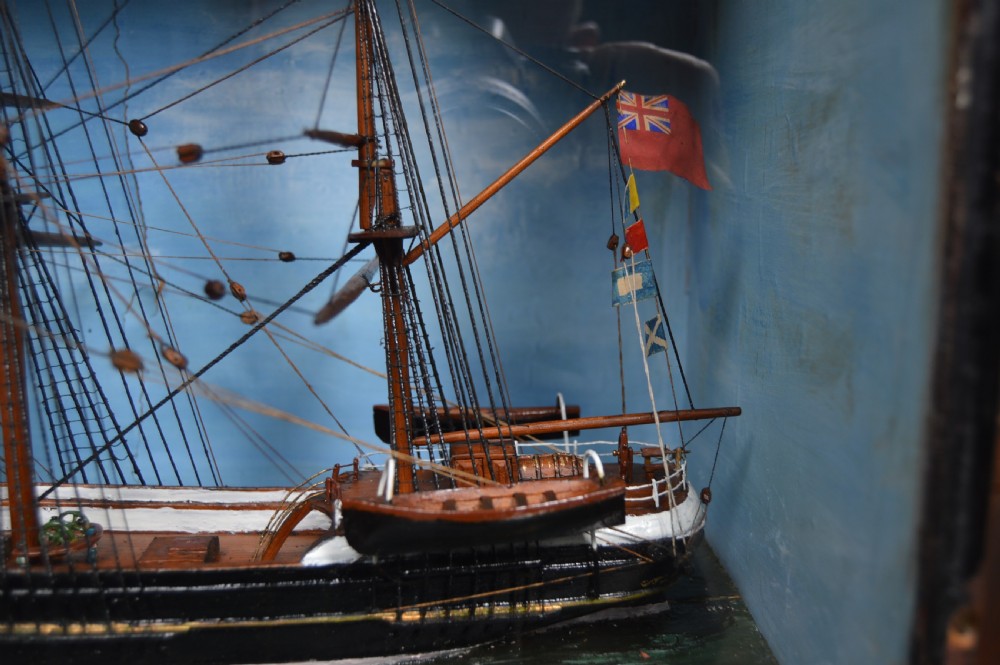 A detailed three-masted clipper ship model with fine thread rigging set against a painted sea and sky inside a black glazed display case. View VI