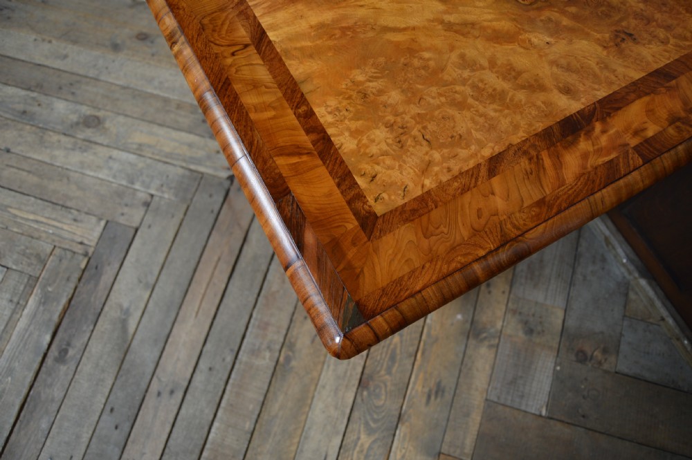 A Victorian burr walnut side table featuring a crossbanded rectangular top, two turned pedestals with a central stretcher, and carved legs with castors. View VIII