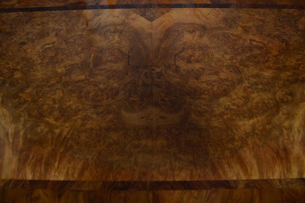 A Victorian burr walnut side table featuring a crossbanded rectangular top, two turned pedestals with a central stretcher, and carved legs with castors. View IX