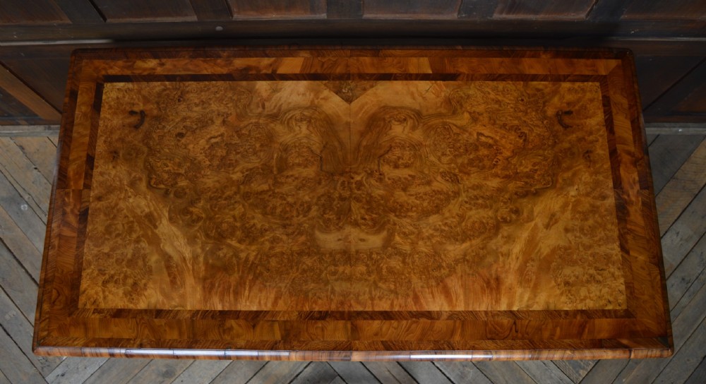A Victorian burr walnut side table featuring a crossbanded rectangular top, two turned pedestals with a central stretcher, and carved legs with castors. View XVIII