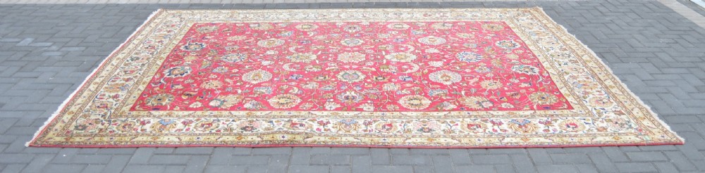 A rectangular handmade Persian wool rug featuring an intricate all-over floral pattern with a dominant red centre and cream borders. View IV