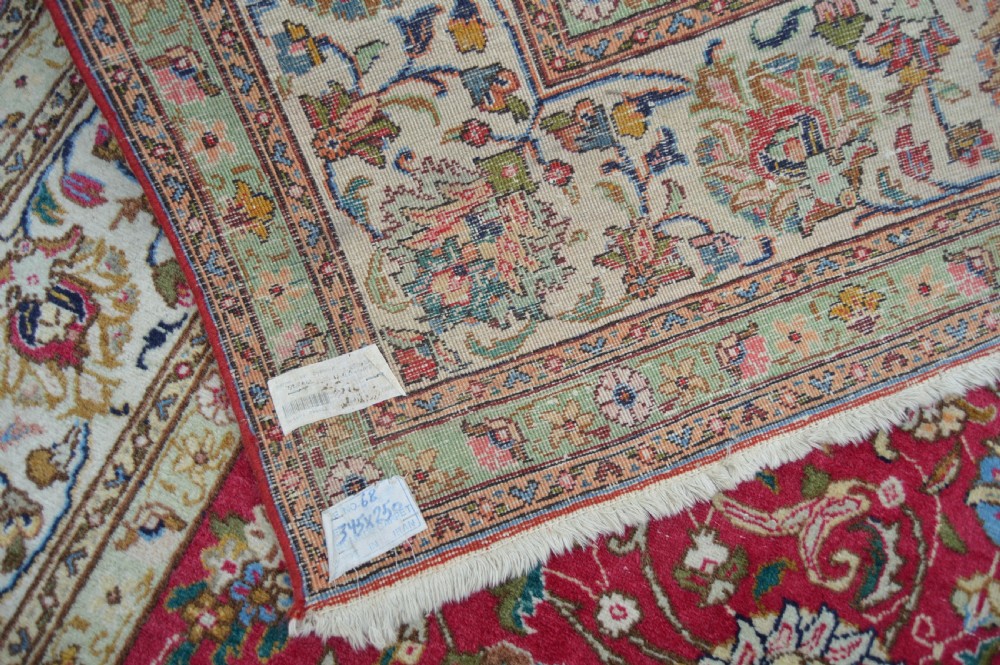 A rectangular handmade Persian wool rug featuring an intricate all-over floral pattern with a dominant red centre and cream borders. View V