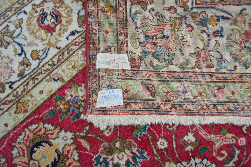 A rectangular handmade Persian wool rug featuring an intricate all-over floral pattern with a dominant red centre and cream borders. View VI