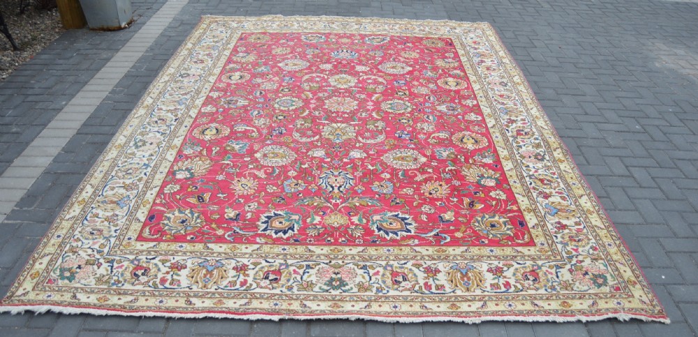 A rectangular handmade Persian wool rug featuring an intricate all-over floral pattern with a dominant red centre and cream borders. View VII
