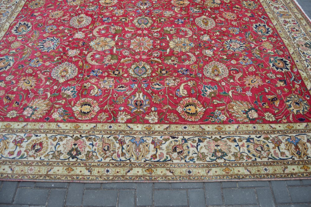 A rectangular handmade Persian wool rug featuring an intricate all-over floral pattern with a dominant red centre and cream borders. View VIII