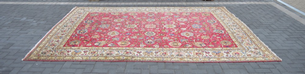 A rectangular handmade Persian wool rug featuring an intricate all-over floral pattern with a dominant red centre and cream borders. View IX