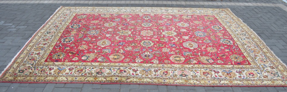 A rectangular handmade Persian wool rug featuring an intricate all-over floral pattern with a dominant red centre and cream borders. View X