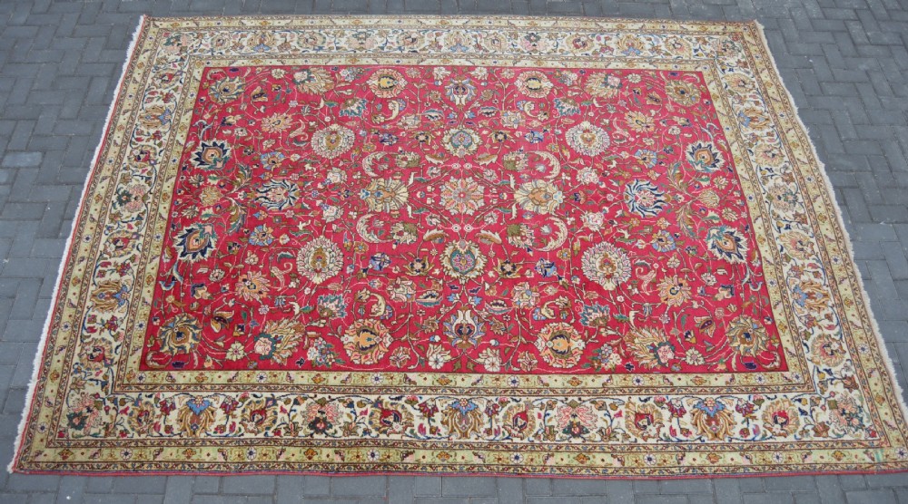 A rectangular handmade Persian wool rug featuring an intricate all-over floral pattern with a dominant red centre and cream borders. View XI
