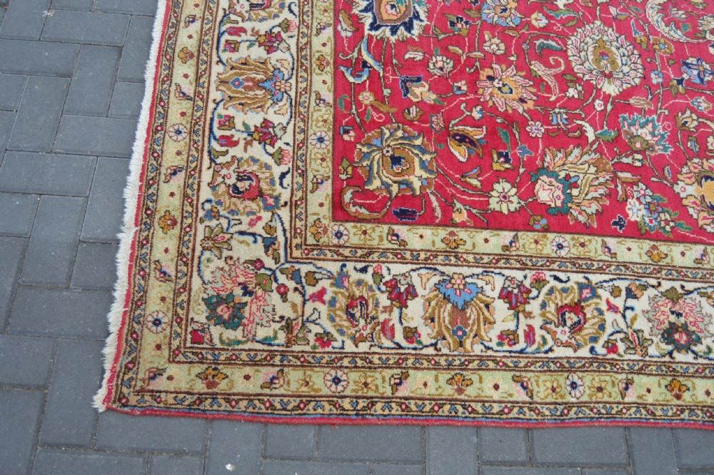 A rectangular handmade Persian wool rug featuring an intricate all-over floral pattern with a dominant red centre and cream borders. View XII