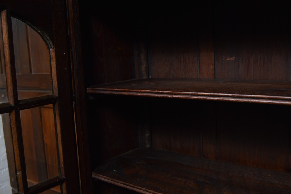 A dark carved oak display cabinet featuring two glazed doors with upper floral carvings and central brass key escutcheons. View XIII