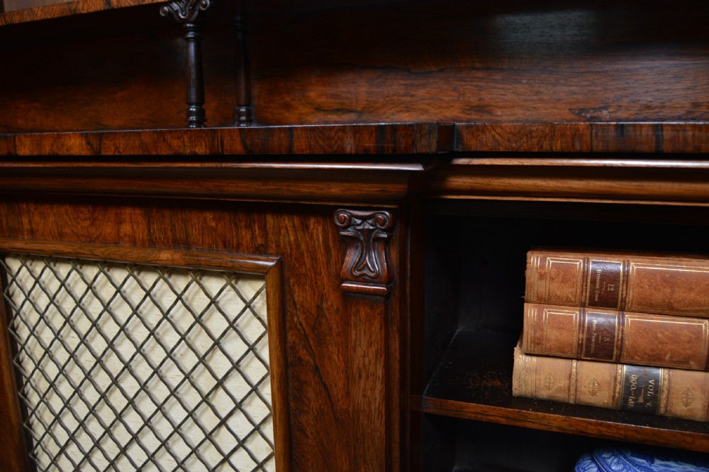 An antique dark rosewood low breakfront bookcase featuring open side shelving, a central door with a brass wire mesh grille, and a raised upper tier topped with a brass gallery. View VIII