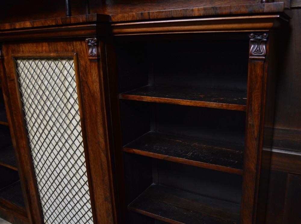 An antique dark rosewood low breakfront bookcase featuring open side shelving, a central door with a brass wire mesh grille, and a raised upper tier topped with a brass gallery. View XV
