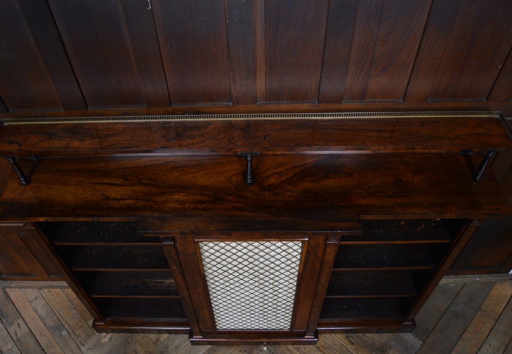 An antique dark rosewood low breakfront bookcase featuring open side shelving, a central door with a brass wire mesh grille, and a raised upper tier topped with a brass gallery. View XVI