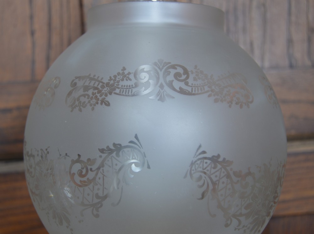 A Victorian brass oil lamp with a black base, fluted column, pink patterned glass reservoir, and frosted glass globe shade with etched detail. View VII