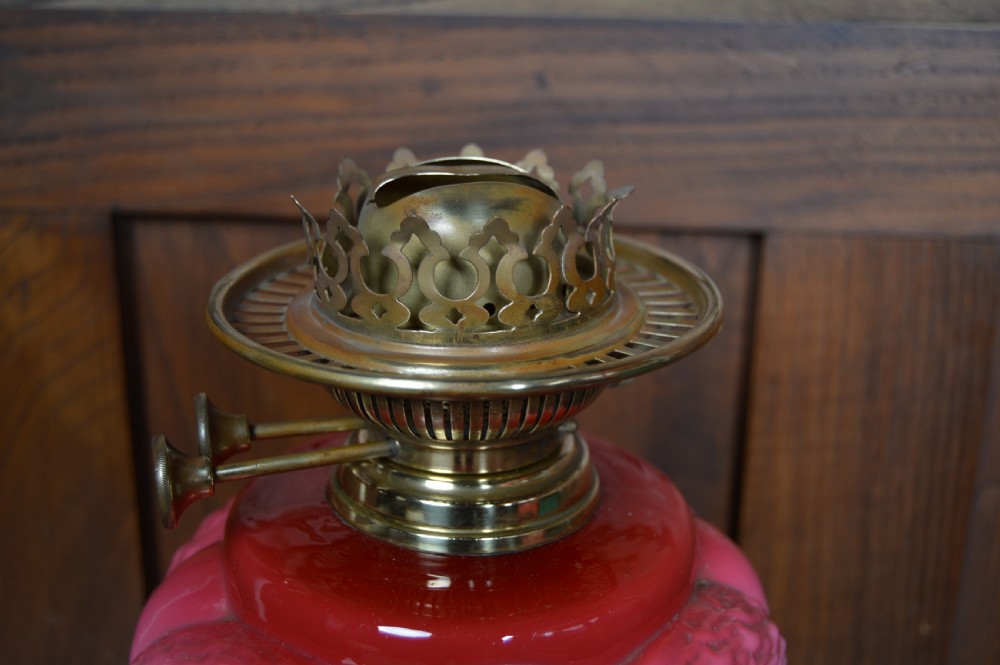 A Victorian brass oil lamp with a black base, fluted column, pink patterned glass reservoir, and frosted glass globe shade with etched detail. View X