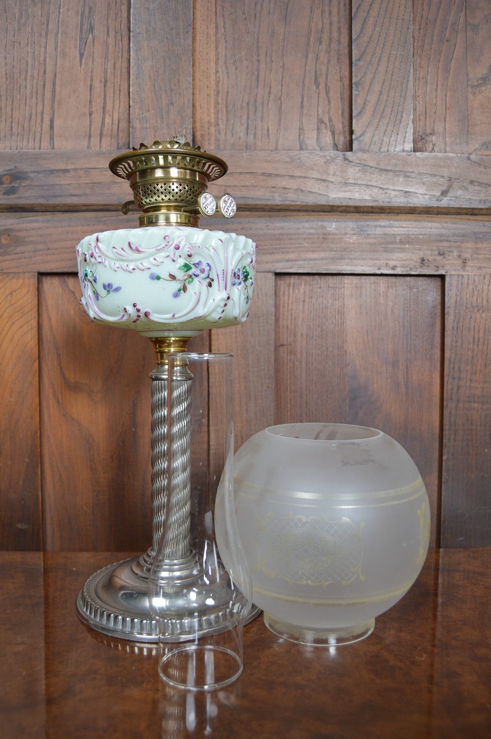 A Victorian Duplex oil lamp featuring an etched glass globe shade, hand-painted floral glass reservoir, spiralled silver-plated column, and stepped round base. View IX
