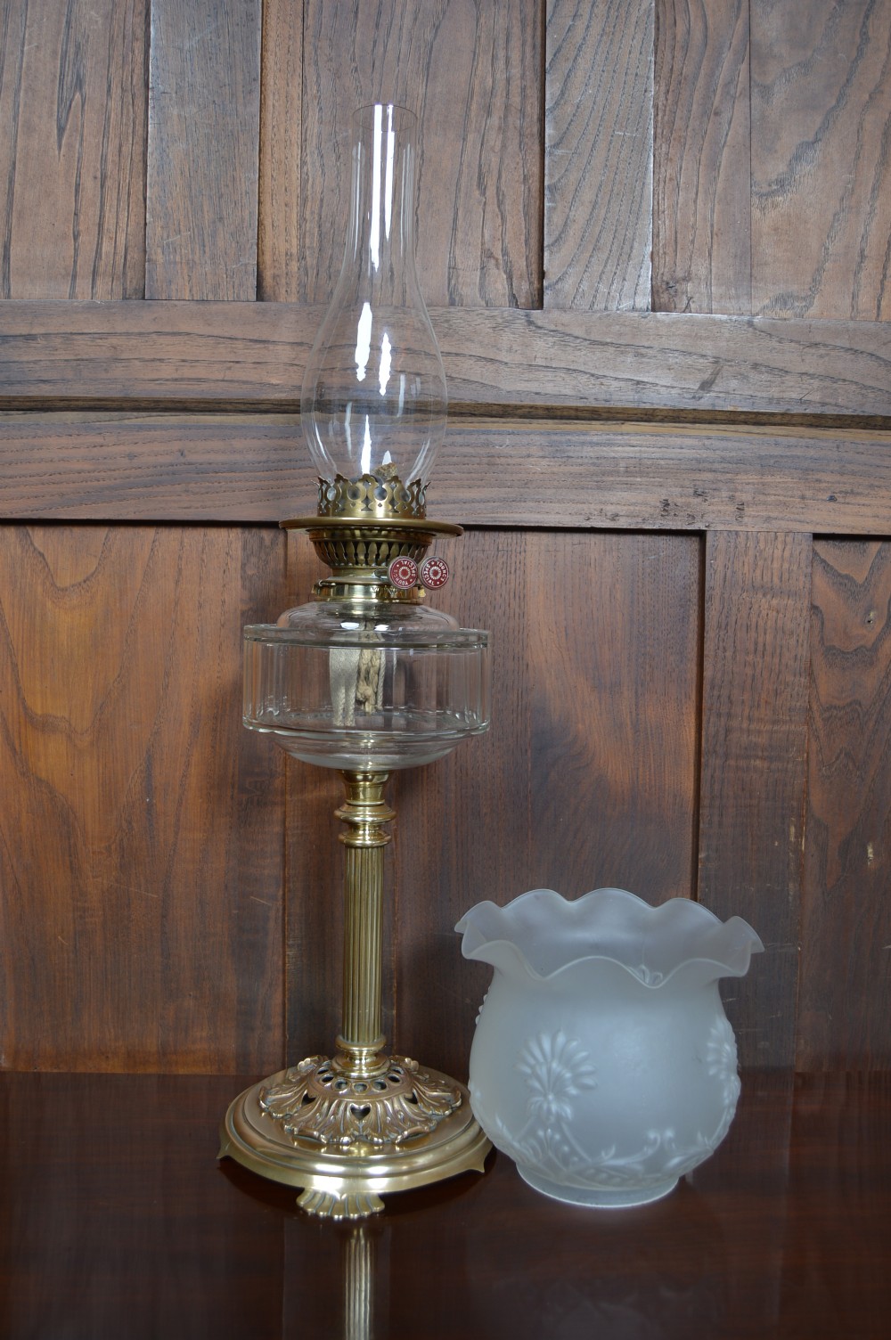 An antique brass paraffin oil lamp featuring a reeded central column, clear glass reservoir, etched frilled glass shade, and clear glass chimney. View VIII
