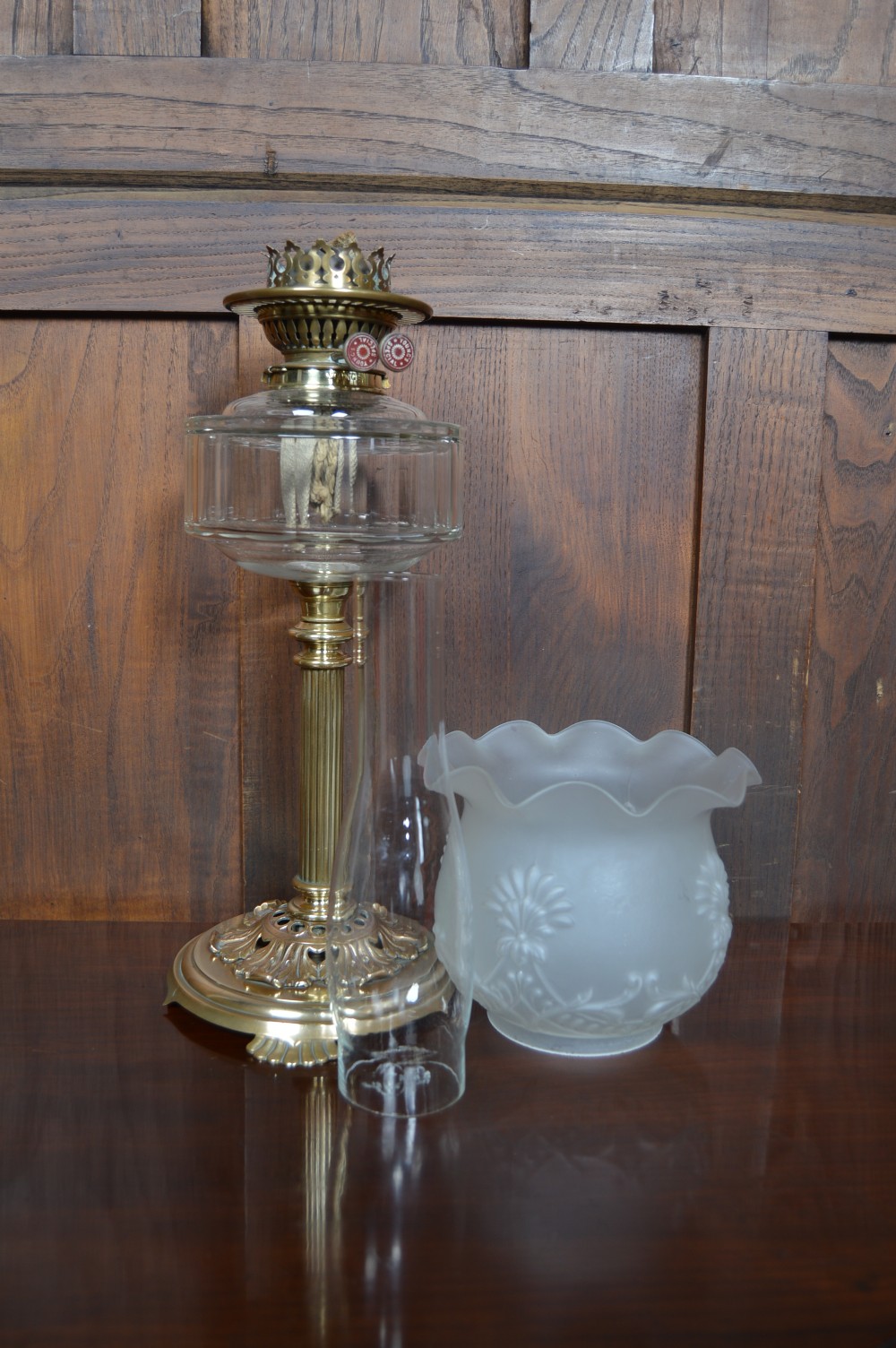 An antique brass paraffin oil lamp featuring a reeded central column, clear glass reservoir, etched frilled glass shade, and clear glass chimney. View IX