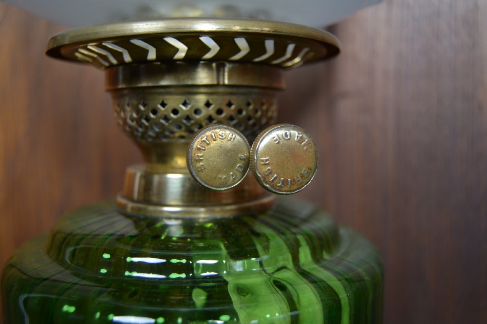 An antique brass paraffin lamp featuring a fluted base, a ribbed green glass reservoir, dual adjustment knobs, and an etched frosted glass shade. View VI