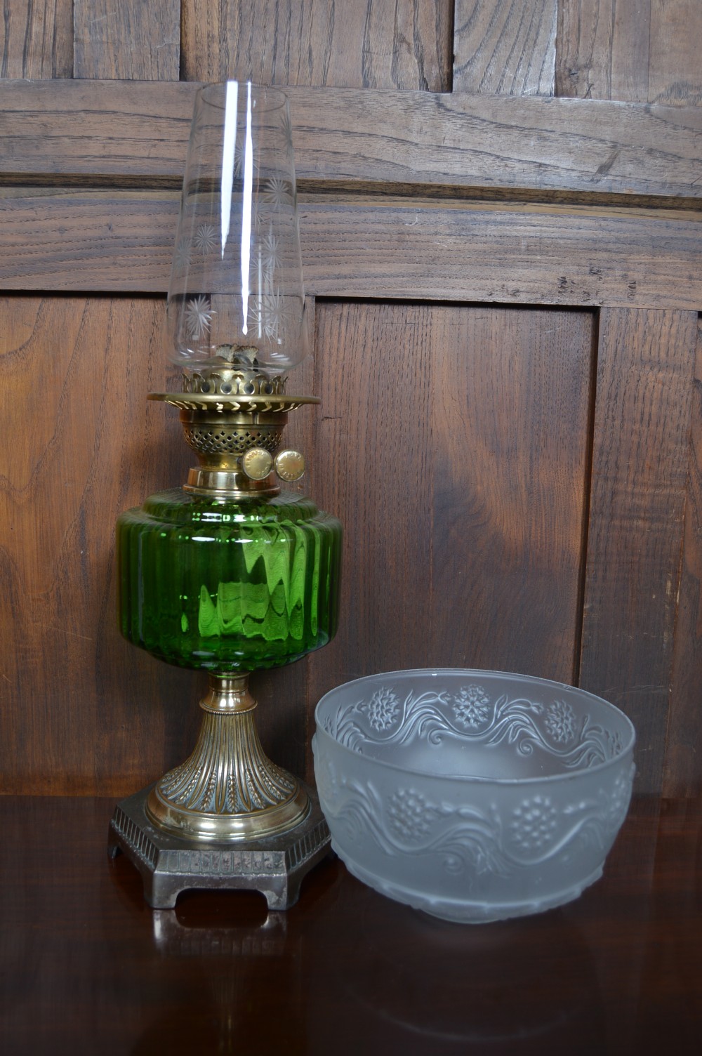 An antique brass paraffin lamp featuring a fluted base, a ribbed green glass reservoir, dual adjustment knobs, and an etched frosted glass shade. View VII