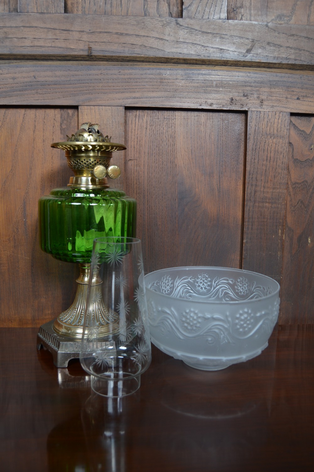 An antique brass paraffin lamp featuring a fluted base, a ribbed green glass reservoir, dual adjustment knobs, and an etched frosted glass shade. View X
