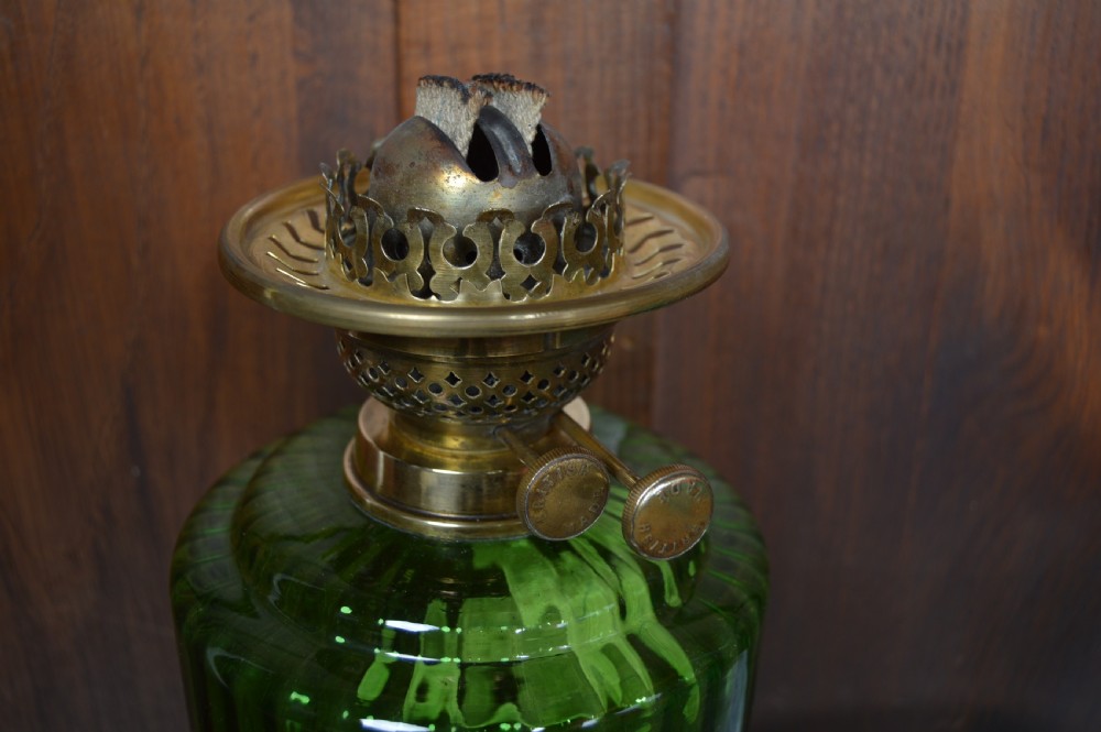 An antique brass paraffin lamp featuring a fluted base, a ribbed green glass reservoir, dual adjustment knobs, and an etched frosted glass shade. View XI