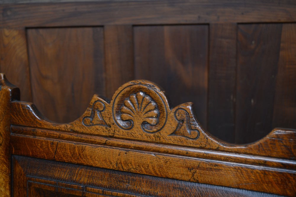 A carved dark oak wainscot style armchair featuring a floral relief panel back, shaped armrests, turned front legs, and wooden stretchers. View II