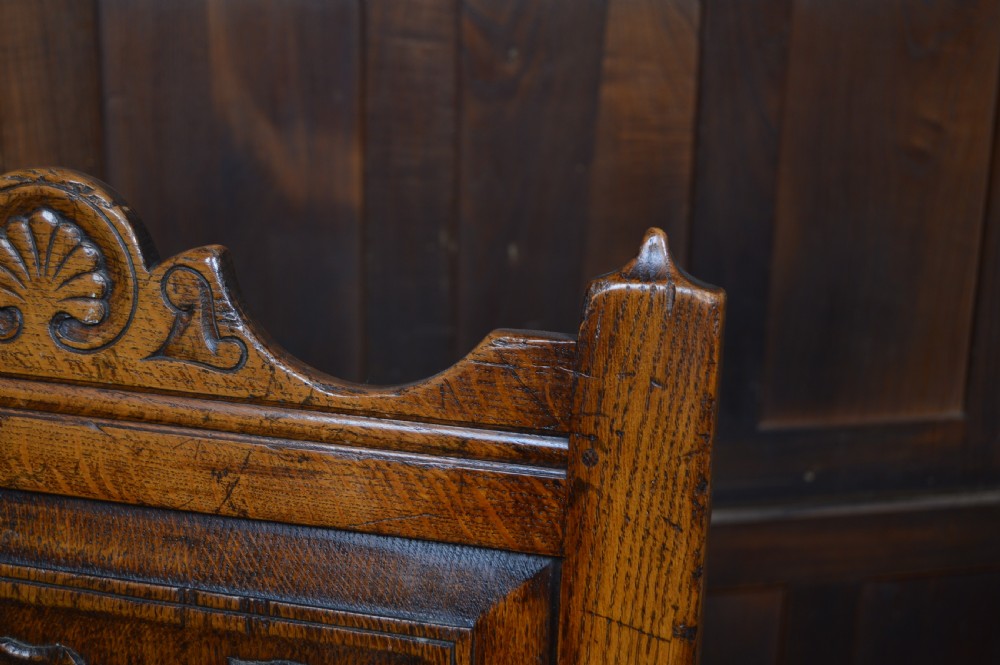 A carved dark oak wainscot style armchair featuring a floral relief panel back, shaped armrests, turned front legs, and wooden stretchers. View III