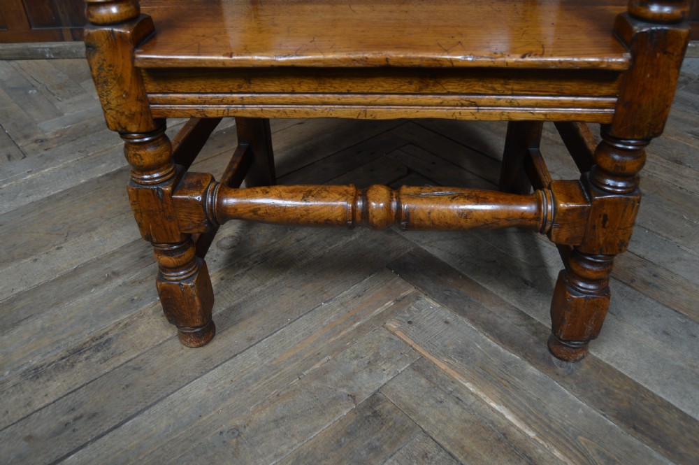A carved dark oak wainscot style armchair featuring a floral relief panel back, shaped armrests, turned front legs, and wooden stretchers. View VII
