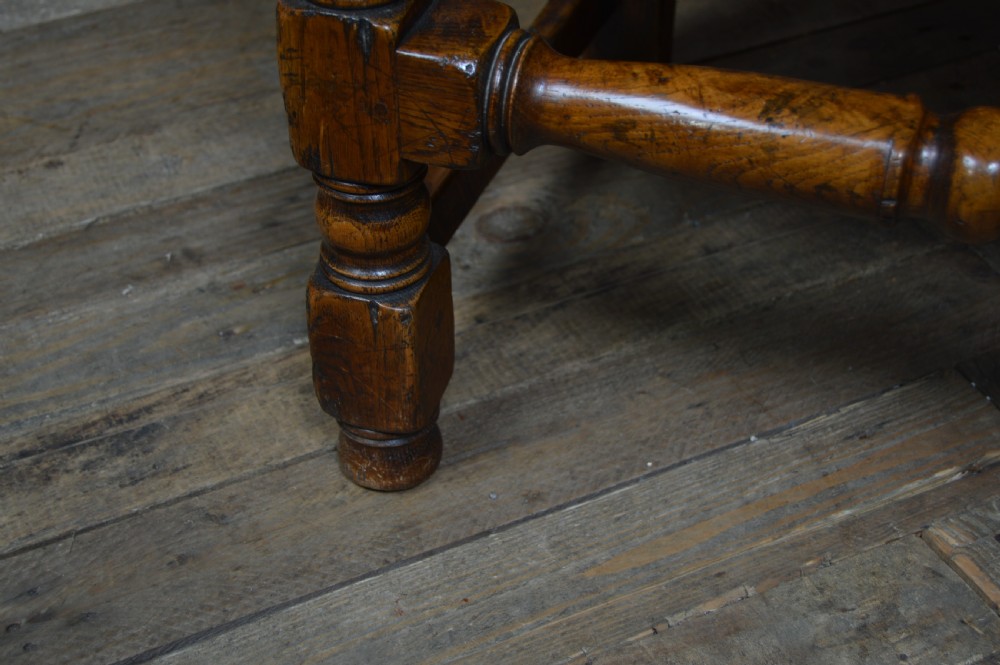 A carved dark oak wainscot style armchair featuring a floral relief panel back, shaped armrests, turned front legs, and wooden stretchers. View VIII